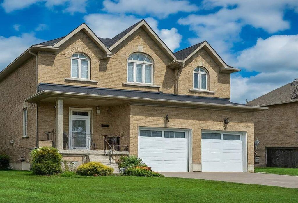 Buying a House in Stittsville. A charming detached home with a two-car garage nestled in a suburban neighbourhood of Stittsville, Ontario. The house boasts a classic design and a manicured lawn, set against a backdrop of a vibrant blue sky dotted with wispy clouds.